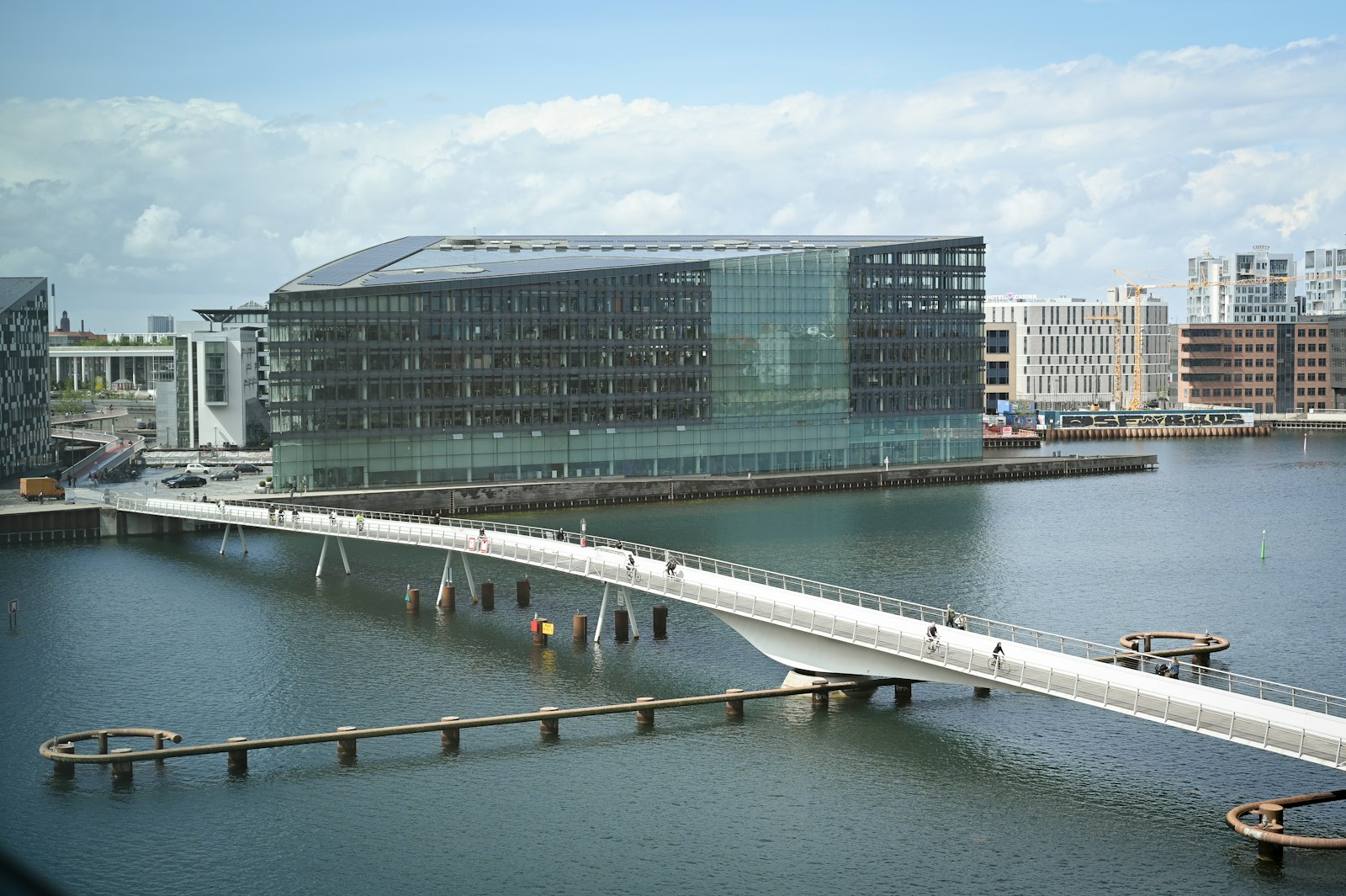 A white pedestrian bridge connects Copenhagen’s modern waterfront across calm blue water.